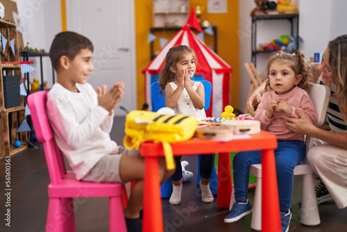 Teacher and group of kids sitting on table applauding at kindergarten