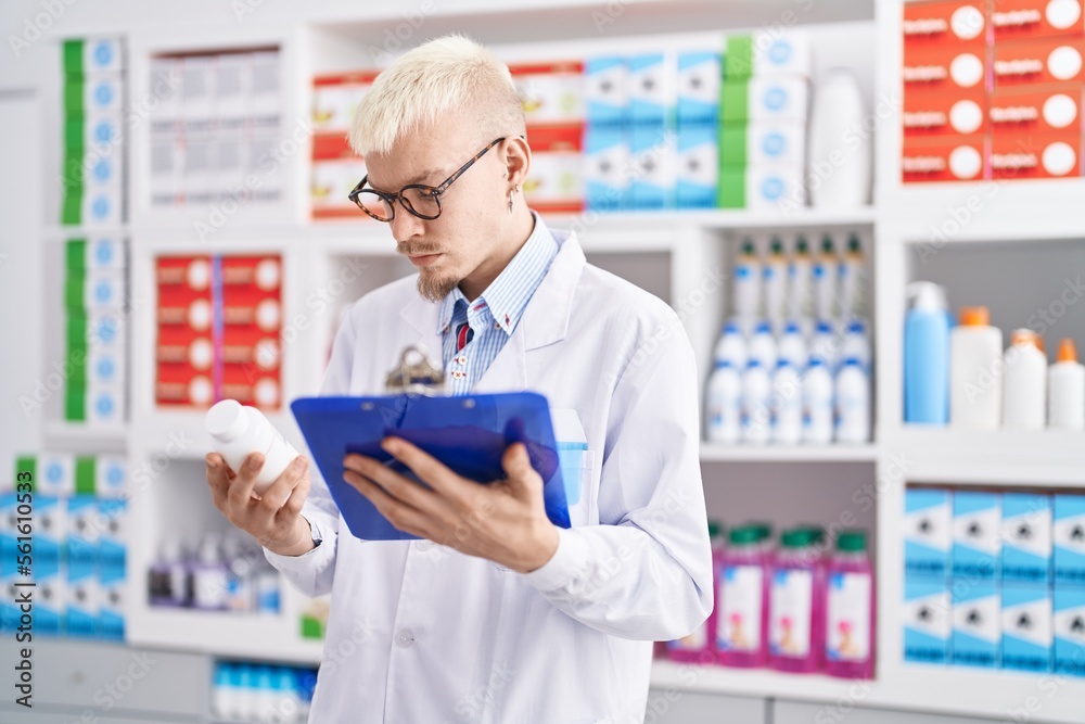 Young caucasian man pharmacist holding pills bottle reading report at pharmacy