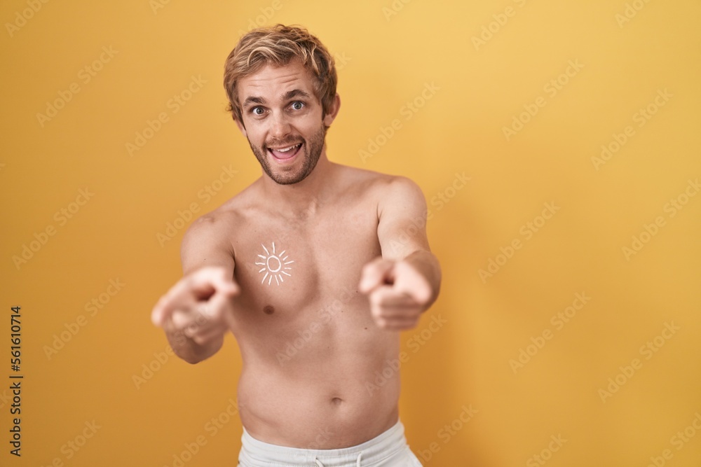 Caucasian man standing shirtless wearing sun screen pointing to you and the camera with fingers, smiling positive and cheerful