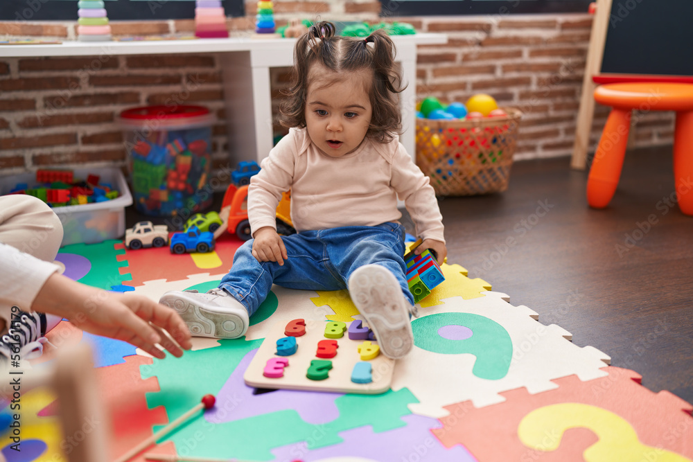Adorable hispanic girl playing with maths puzzle game sitting on floor at kindergarten Adorable hispanic girl playing with maths puzzle game sitting on floor at kindergarten