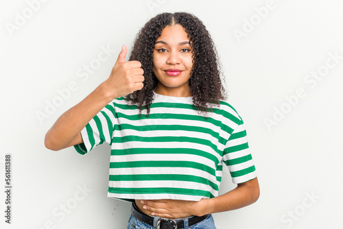 Young african american woman isolated on white background touches tummy, smiles gently, eating and satisfaction concept.