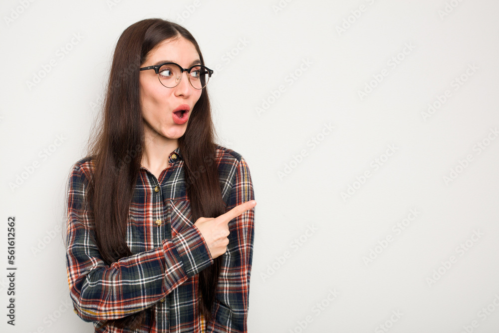 Young caucasian woman isolated on white background points with thumb finger away, laughing and carefree.