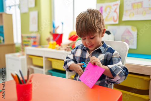 Adorable hispanic boy student smiling confident cutting paper at kindergarten