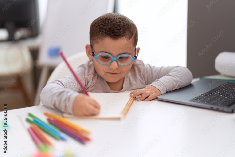 Adorable hispanic toddler student using laptop drawing on notebook at classroom Adorable hispanic toddler student using laptop drawing on notebook at classroom