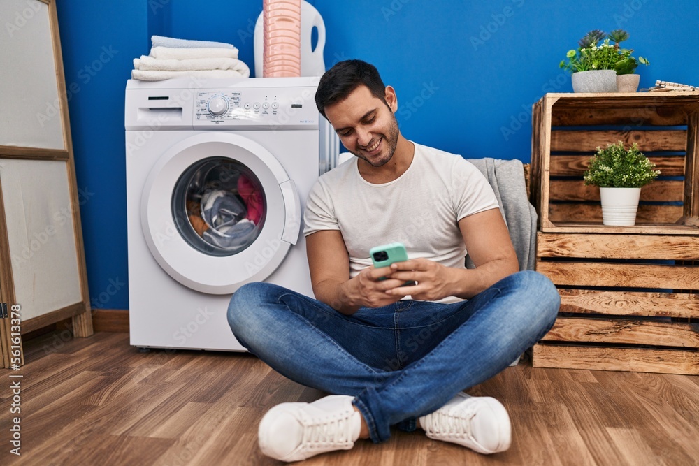 Young hispanic man using smartphone waiting for washing machine at laundry room Young hispanic man using smartphone waiting for washing machine at laundry room