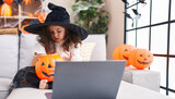 Adorable hispanic girl wearing halloween costume using laptop at home
