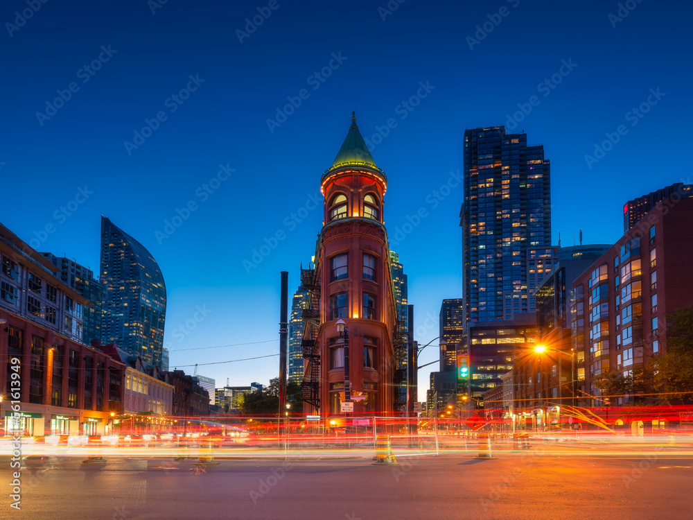Canada, Toronto. The famous Gooderham building and the skyscrapers in the background. View of the city in the evening. Blurring traffic lights. Modern and ancient architecture. Night city.