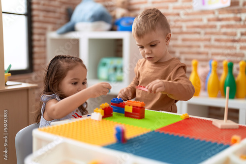 Adorable girl and boy playing with construction block pieces sitting on table at kindergarten