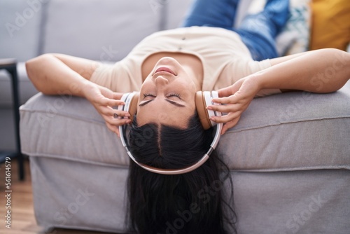 Young beautiful hispanic woman listening to music lying on sofa at home