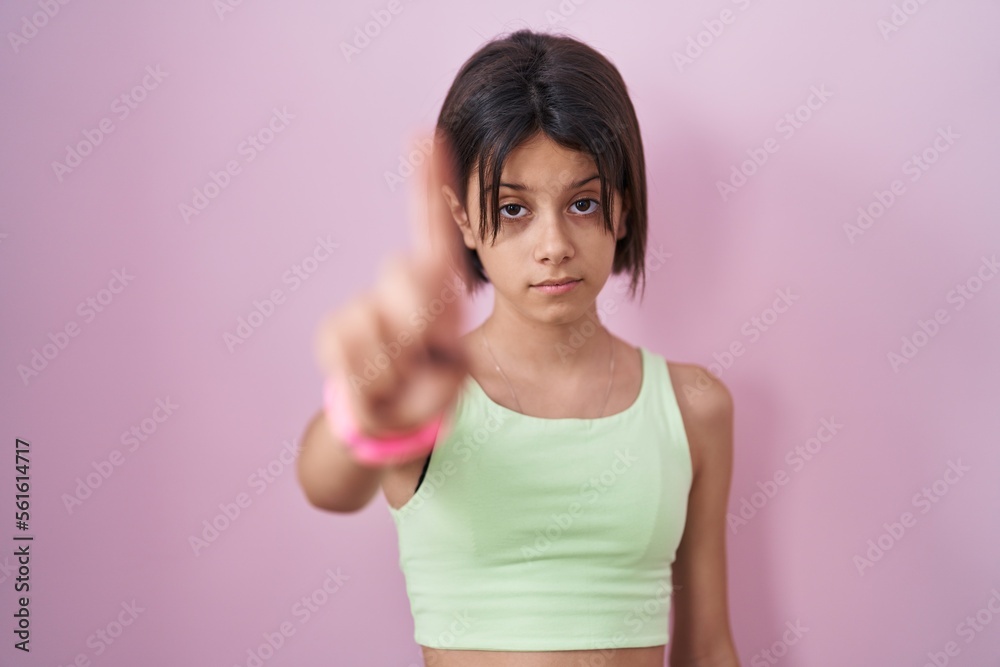 Young girl standing over pink background pointing with finger up and angry expression, showing no gesture Young girl standing over pink background pointing with finger up and angry expression, showing no gesture
