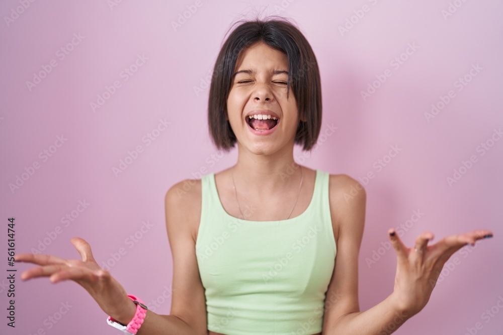 Φωτογραφία Young girl standing over pink background celebrating mad and crazy for success with arms raised and closed eyes screaming excited