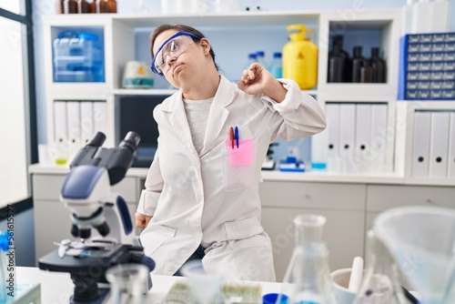 Hispanic girl with down syndrome working at scientist laboratory stretching back  tired and relaxed  sleepy and yawning for early morning