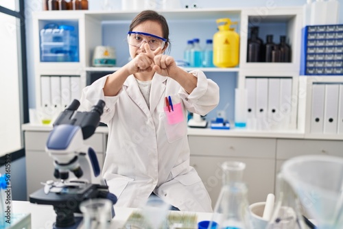 Hispanic girl with down syndrome working at scientist laboratory rejection expression crossing fingers doing negative sign