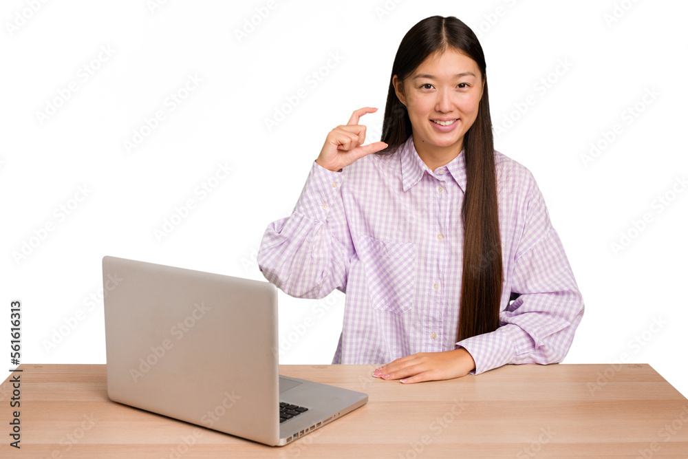 Φωτογραφία Young student asian woman in a workplace with a laptop isolated holding something little with forefingers, smiling and confident
