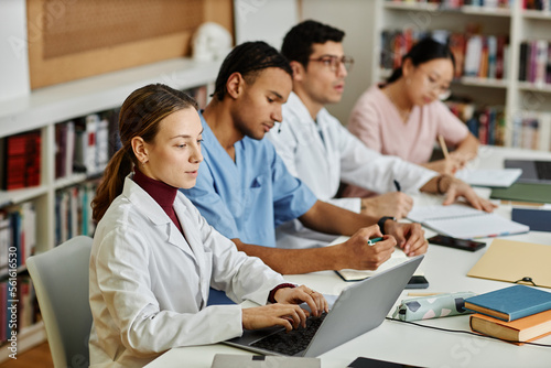 Diverse group of young med students sitting in row at table during lecture or seminar