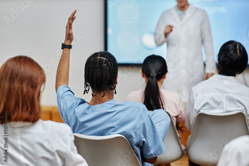 Tableau sur toile Back view at young black doctor raising hand in audience at medical seminar, cop