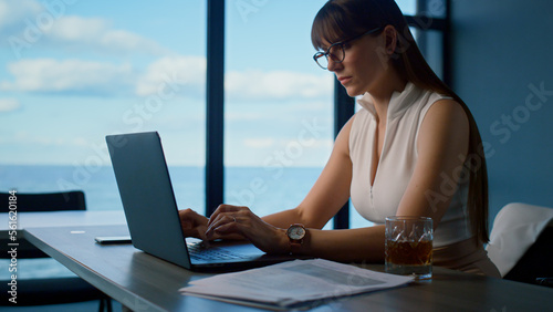 Woman professional surfing laptop at sea panorama window. Office manager working