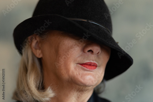 Studio portrait of a mature lady in a black hat pulled over her eyes © Guzel