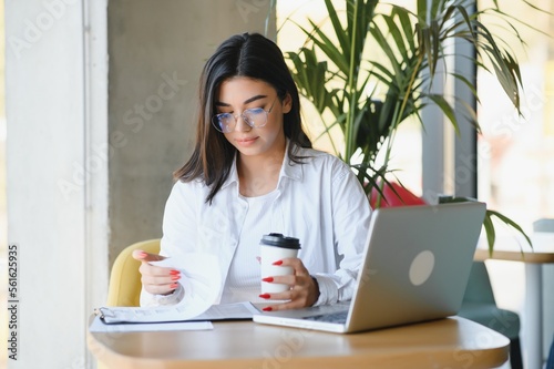 Young charming female freelancer using laptop computer for distance job while sitting in modern coffee shop interior, beautiful Caucasian woman working on net-book during morning breakfast in cafe bar
