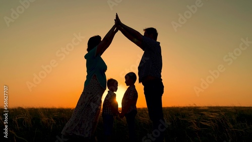 Symbol of house with their own hands, silhouette at sunset, children, mom and dad, play together. Parental care for children. Happy family dreaming about their own house in park in summer in sun
