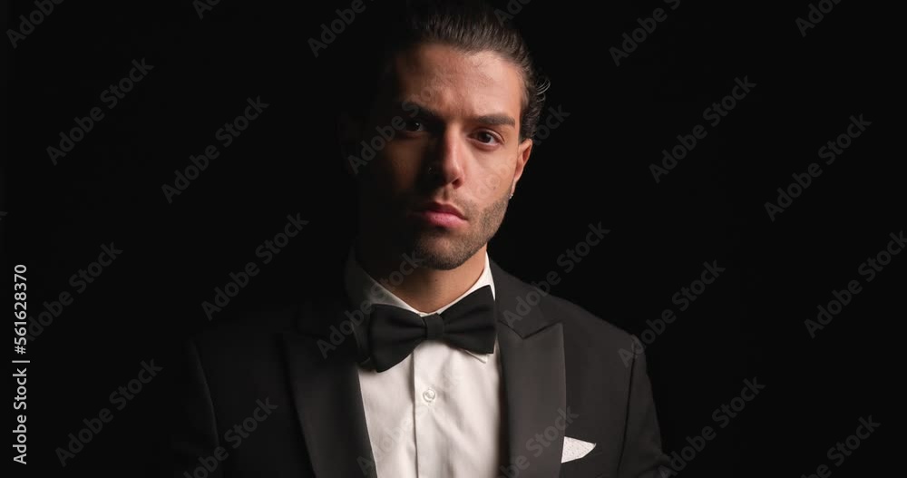 sexy Arabic man fixing tuxedo and bowtie, smiling while pointing finger and inviting in front of black background sexy Arabic man fixing tuxedo and bowtie, smiling while pointing finger and inviting in front of black background