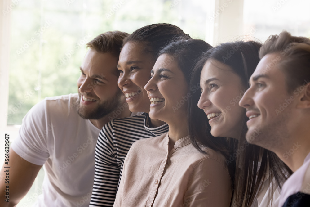 Obraz premium Diverse united team sitting close in line, looking away, smiling, laughing, posing for shooting, celebrating teamwork success. Multiethnic friends enjoying leisure, friendship