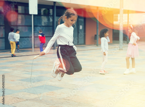 Tableau sur toile Cheerful sporty tween girl jumping rope in school yard during recess in warm aut