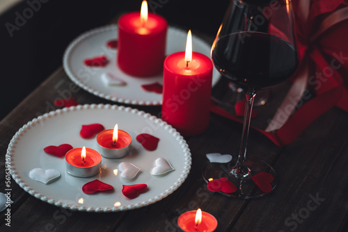 Saint Valentine's Day celebration. Red burning candles, hearts, gift box, postcard on dark wooden background. Happy holiday . Table decor for festive dinner, romantic atmosphere photo