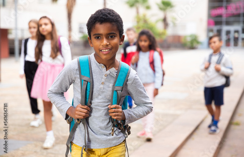 Portrait of african american boy standing near school, children on background