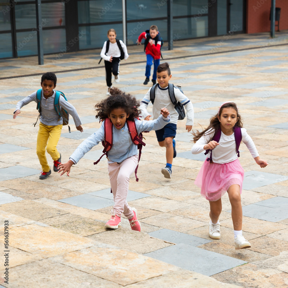 Portrait of cheerful tween boys and girls with school backpacks running in schoolyard in spring day.