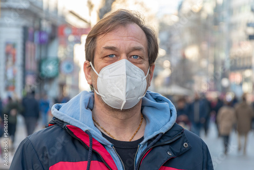 Street Portrait of a 45-50-year-old man in a medical mask against the background of a city street and a crowd of people, looking into the camera. Concept: wearing a mask in quarantine, air pollution, 