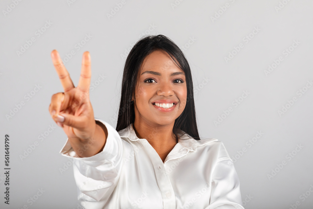 Smiling confident pretty millennial black female in white blouse show peace sign, enjoy good deal Smiling confident pretty millennial black female in white blouse show peace sign, enjoy good deal