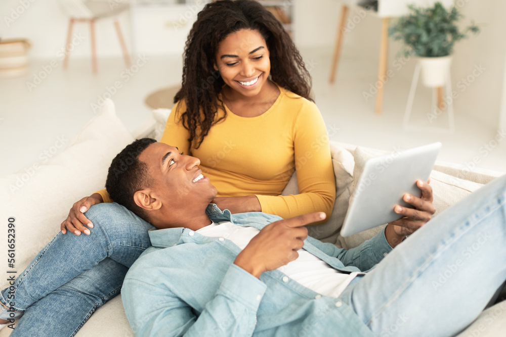 Glad young african american guy shows tablet to lady, recommends website and app, rest and relax together Glad young african american guy shows tablet to lady, recommends website and app, rest and relax together