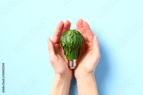 Female hands holding lightbulb decorated with green leaves. Concept of ecology, green power, saving the planet and eco-friendly living.