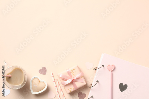 Valentine's Day flat lay composition with gift box, coffee cup, candles, paper photo album, hearts on beige background.