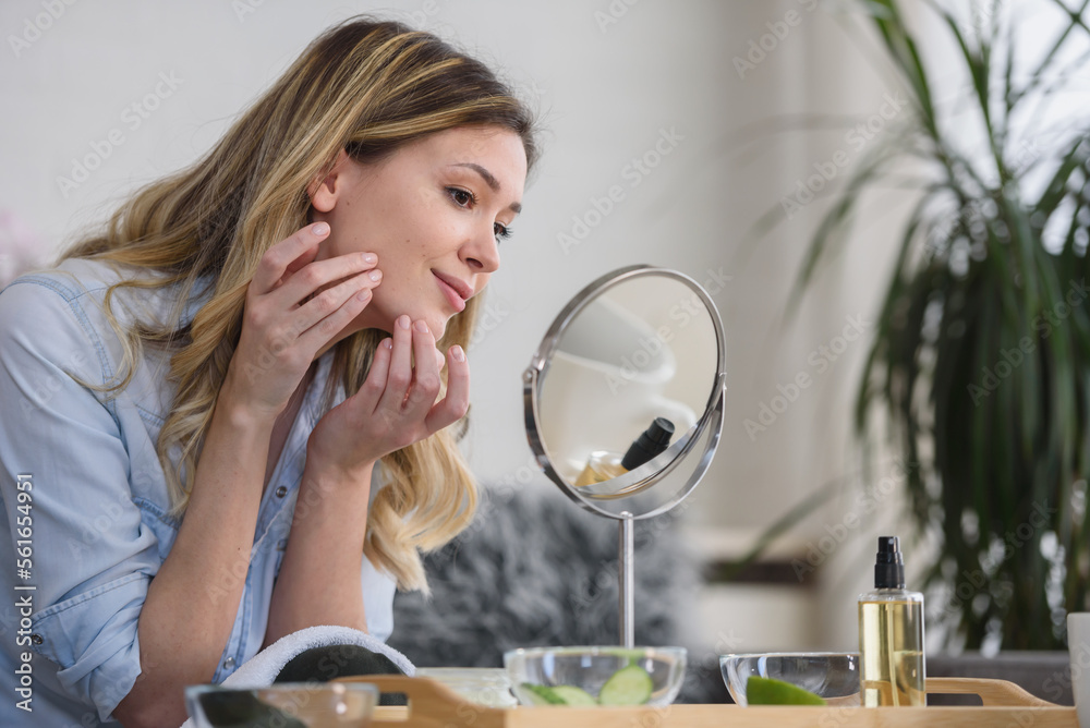 Young woman looking herself in the mirror at home. Worried about acne caused by wearing a mask. Maskne. Problems with acne.
