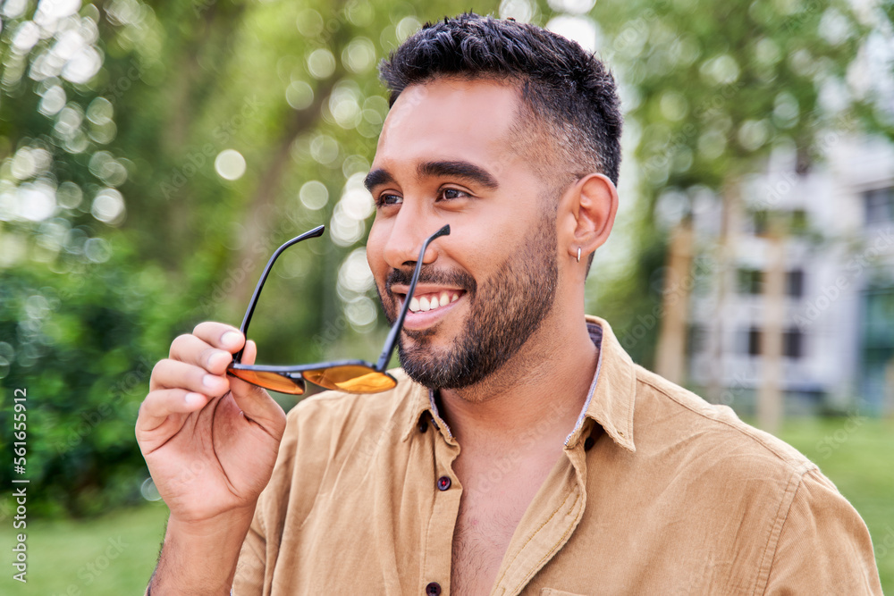 portrait of a young latin man with sunglasses in hand and beard smiling portrait of a young latin man with sunglasses in hand and beard smiling