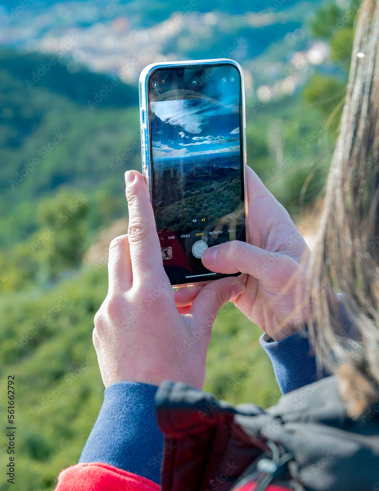 Joven mujer tomando fotos con su teléfono móvil desde lo alto de la montaña.