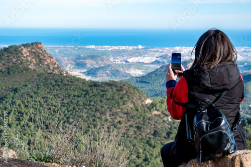 Joven mujer tomando fotos con su teléfono móvil desde lo alto de la montaña. photo