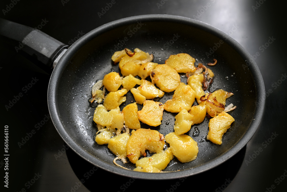 Potato slices and onion are roasted in a black frying pan on the stove, in Germany called Bratkartoffeln, food and cooking theme, selected focus Potato slices and onion are roasted in a black frying pan on the stove, in Germany called Bratkartoffeln, food and cooking theme, selected focus