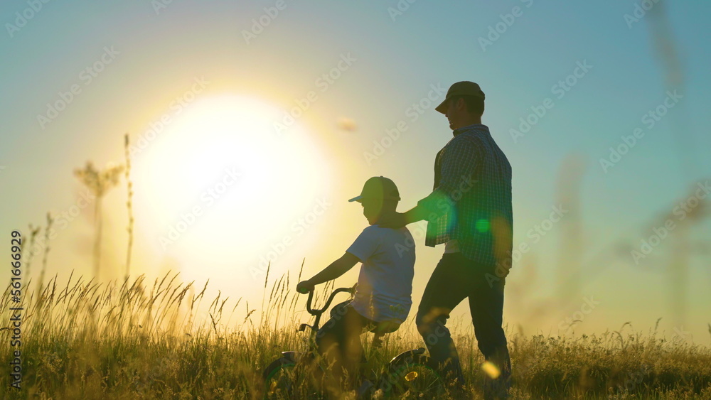 Active family, dad teaches his son to ride bike in park at sunset. Father teaches little boy to ride childrens bicycle on road in countryside in sun. Happy family, childhood. Daddy plays outside