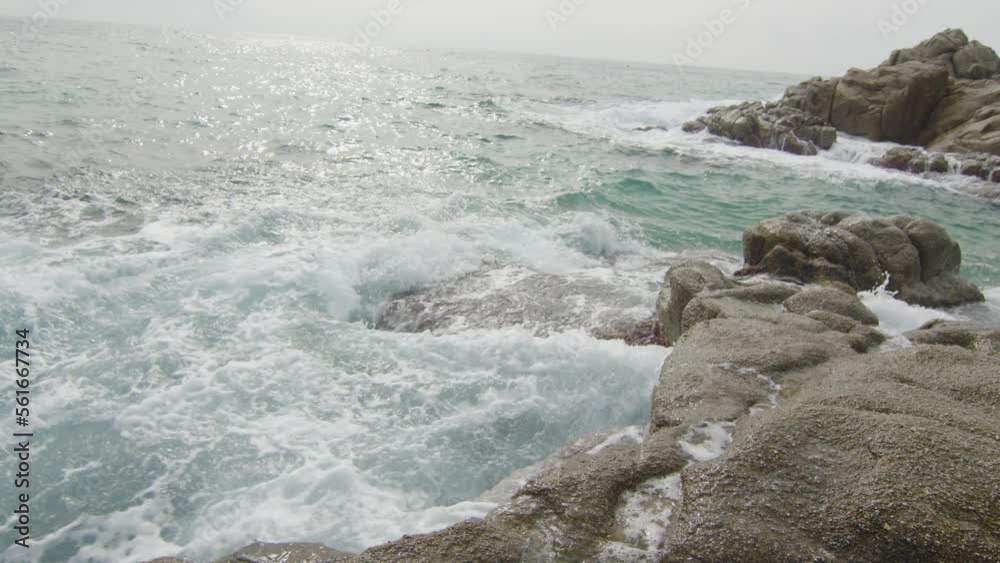 Waves splash on the rocks at the edge of the sunny beach, in Spain Waves splash on the rocks at the edge of the sunny beach, in Spain
