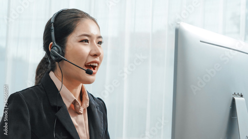 Asian customer support operator wearing headset and microphone working at her desk with laptop. Enthusiastic female employee provide customer service, supportive call center agent helping customers.