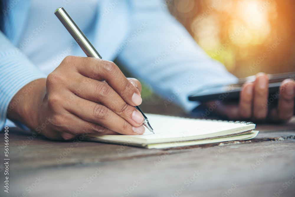 Man hands writing notebook diary with coffee cup and smartphone on wood desk. Close up man hands using pen sitting at wooden table outdoors lifestyle. Men write planner note diary office agenda Man hands writing notebook diary with coffee cup and smartphone on wood desk. Close up man hands using pen sitting at wooden table outdoors lifestyle. Men write planner note diary office agenda