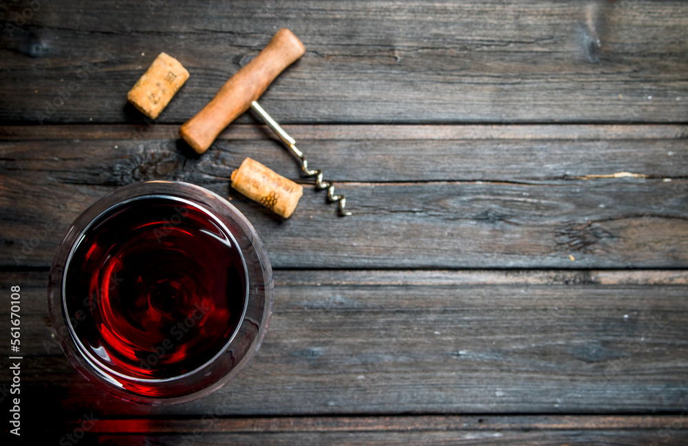 glass of red wine with a corkscrew and corks.
