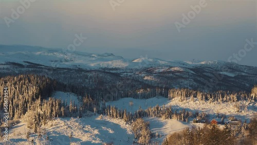 Aerial wide shot of Beautiful snowy landscape with icy forest trees during golden sunset in Norway photo