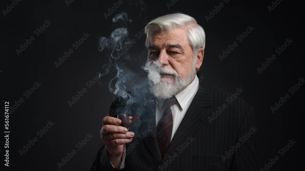 Close-up shot of thoughtful, serious man using matches to smoke a pipe with tobacco. Portrait of an adult gentleman enjoying smoking indoors. High quality 4k footage