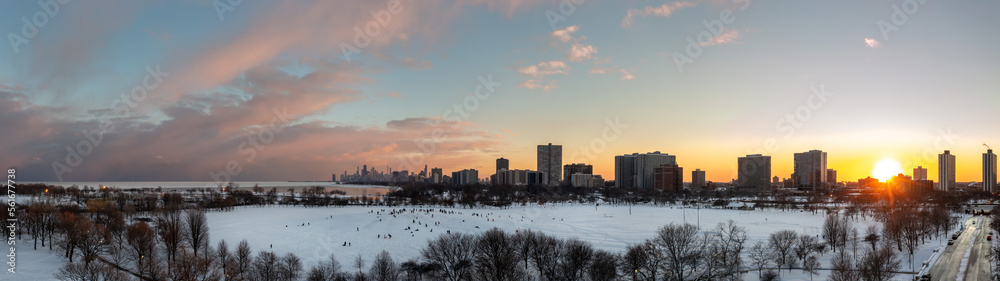 Fototapeta premium Beautiful sunset aerial panorama of cricket hill with the sun setting behind residential highrise buildings in the Uptown neighborhood with the downtown skyline in the distance and pink clouds above.