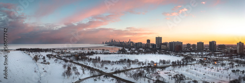 Beautiful Chicago winter skyline aerial above a snow covered Montrose beach looking towards the downtown skyscraper buildings with pink and orange clouds in a blue sky above.