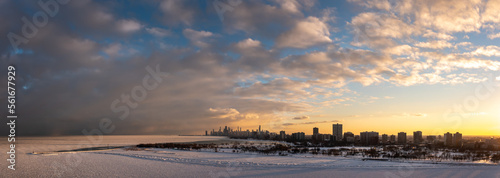 Wide angle aerial panorama of the north side of Chicago from above the frozen water of Lake Michigan overlooking the Uptown and Lakeview neighborhoods towards downtown at sunset with cloudy sky above.